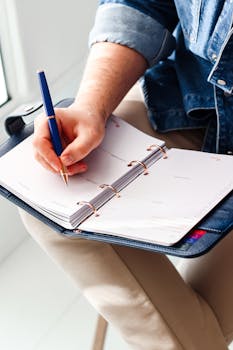 Focused image of a hand writing in a planner for schedule organization.